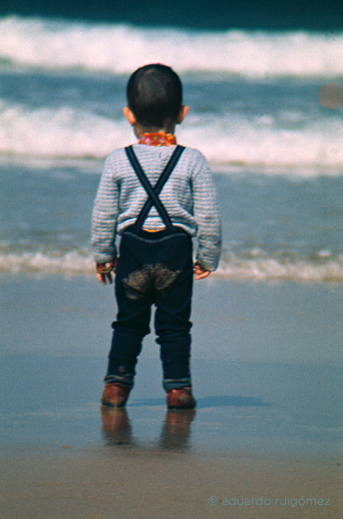 Niño en la orilla de una playa contemplando el mar.