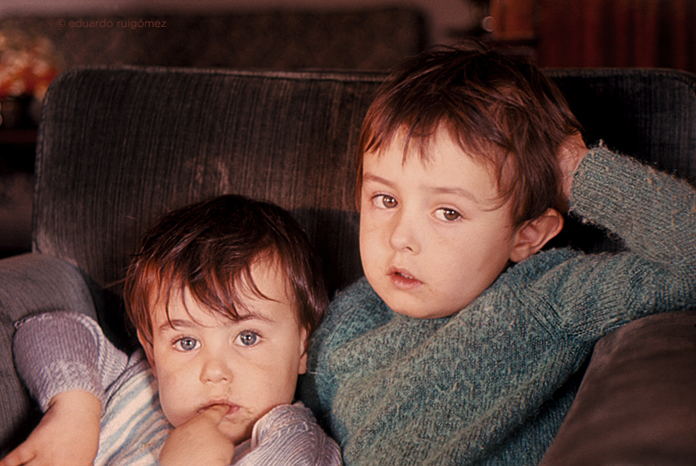 Dos niños sentados en un sofá mirando a la cámara.