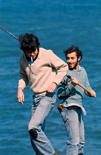 Chicos pescando con caña en la costa.