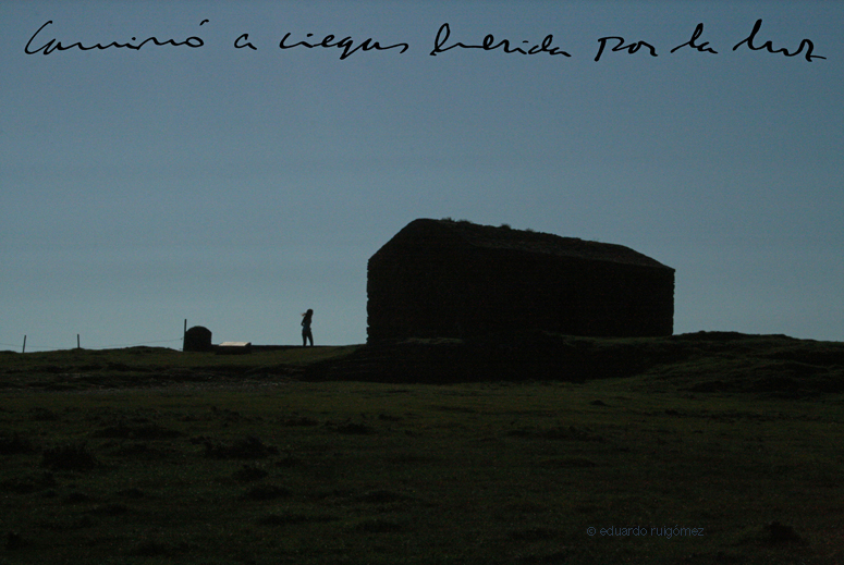 Silueta de mujer joven en el horizonte a contraluz, junto a una cabaña al borde de un acantilado en La Coruña.