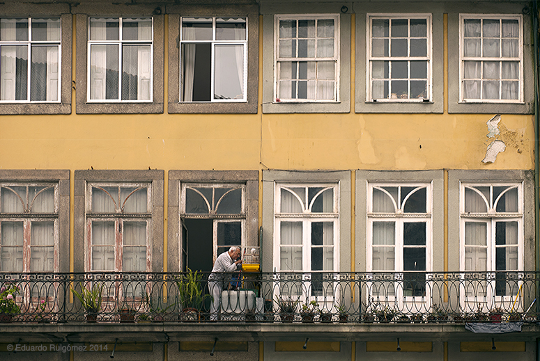 Un hombre en la terraza da de comer a su pájaro enla jaula