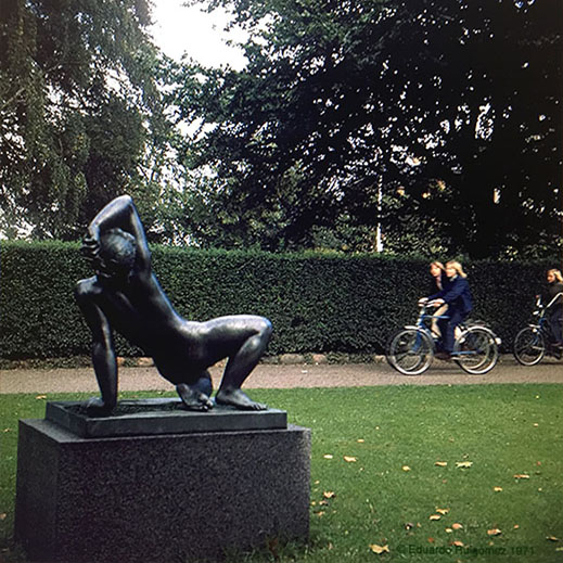 Tres muchachas pasean por un parque frente a una escultura.