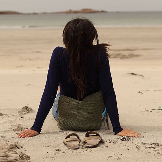 Una chica sentada mirando hacia la orilla de una playa