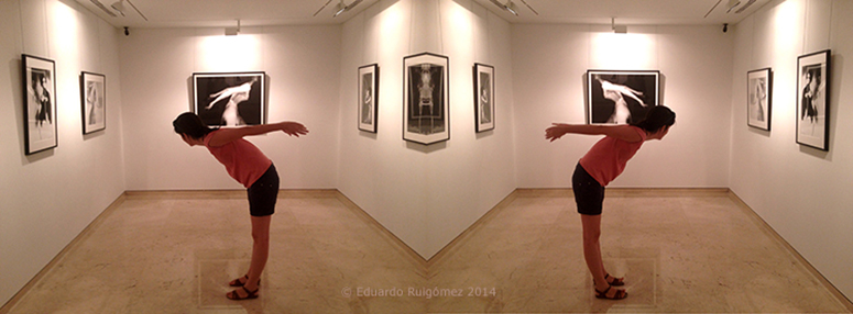 Chica alzando los brazos hacia atrás imitando a una fotografía de Lillian Bassman en el fondo de la sala de exposiciones.