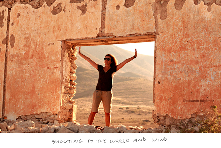 Mujer con los brazos alzados en el marco de una ventana de las ruinas de un fortín militar.
